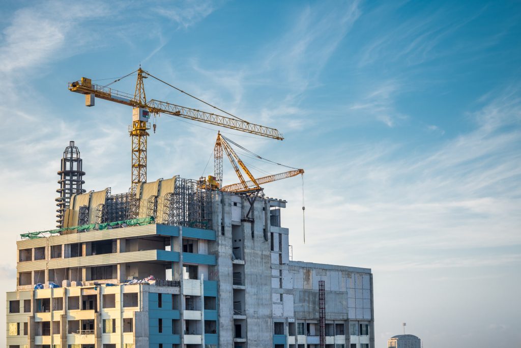 A construction site with a partially built high-rise building and a crane against a clear blue sky.